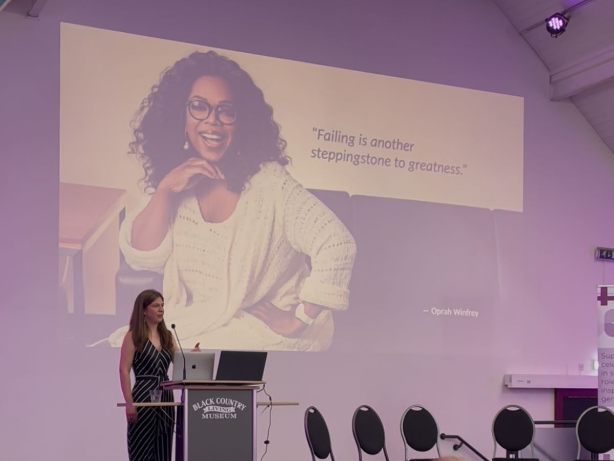 An image of Gabrielle Lawrence, at the Black Country Living Museum's stage, standing behind a podium, behind her is a projected presentation showing Oprah Winfrey with a quote "Failing is another stepping stone to greatness"
